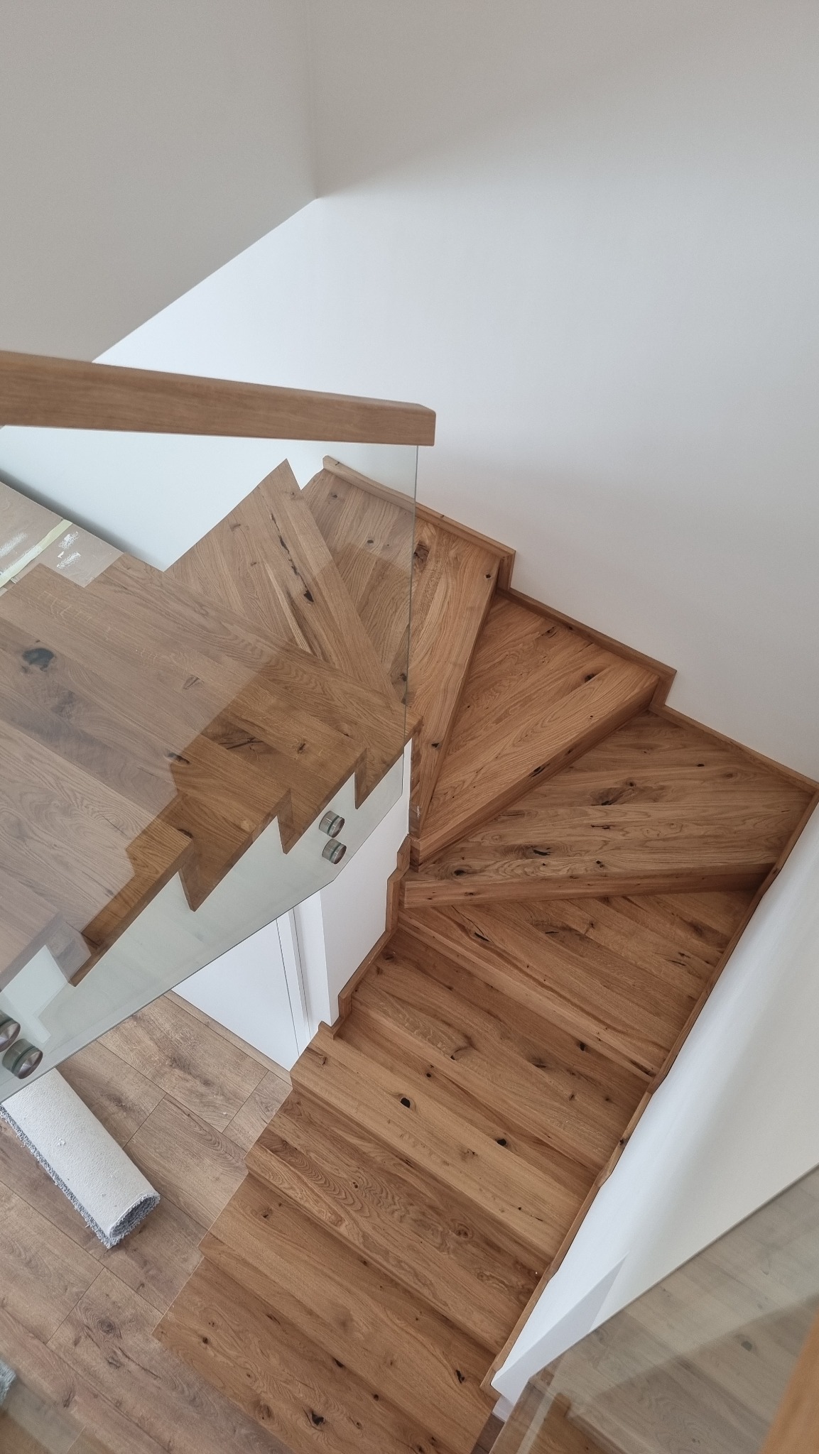 Nowoczesne schody z drewna dębowego z balustradą ze szkła hartowanego, widok z góry na stopnie z wyraźnym usłojeniem i minimalistyczne mocowania szkła.