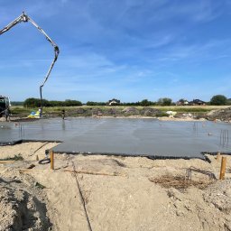 KP Budownictwo - Wylewanie fundamentów pod budynek jednorodzinny za pomocą pompy do betonu na tle błękitnego nieba.