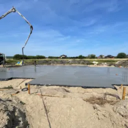 Wylewanie fundamentów pod budynek jednorodzinny za pomocą pompy do betonu na tle błękitnego nieba.