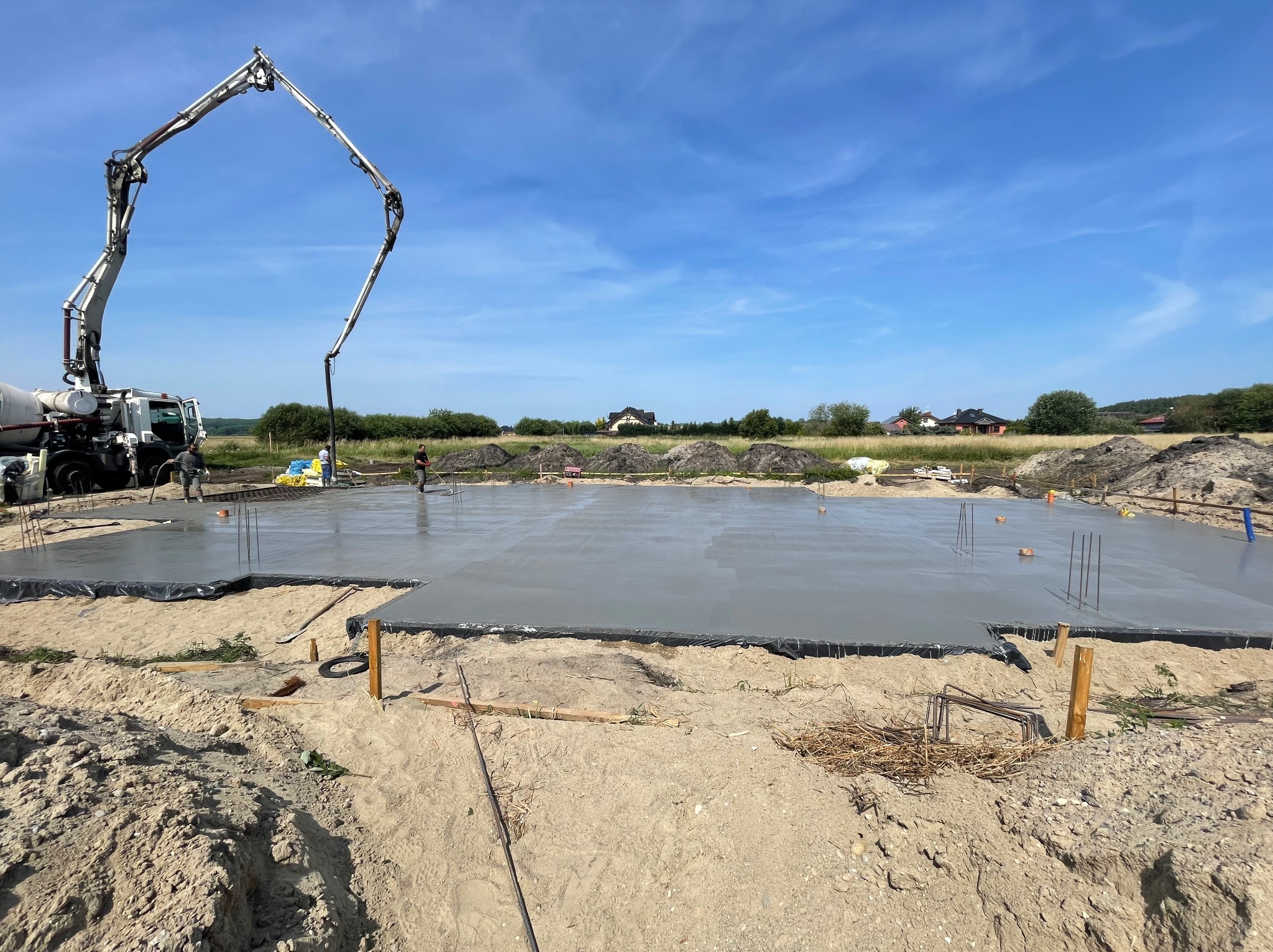 Wylewanie fundamentów pod budynek jednorodzinny za pomocą pompy do betonu na tle błękitnego nieba.