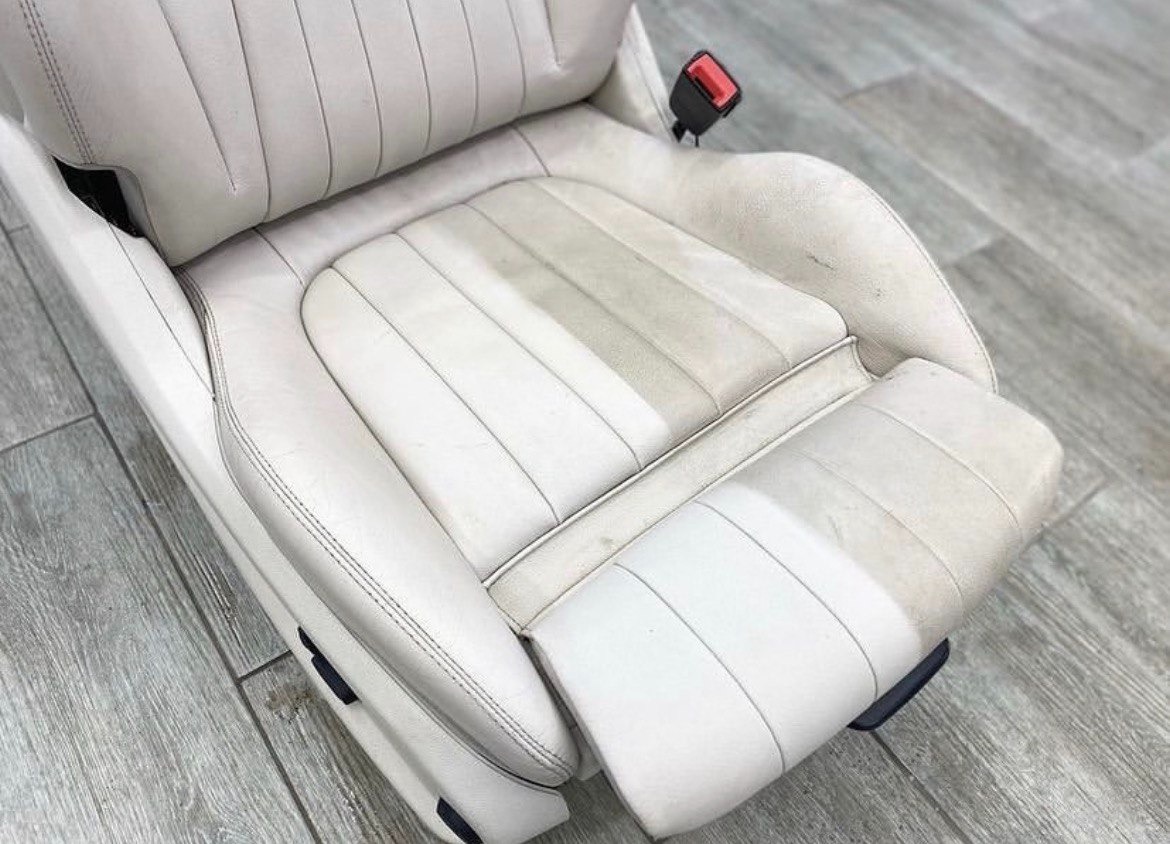 Biały, skórzany fotel samochodowy z widocznymi plamami i różnicą w czystości po częściowym czyszczeniu, ukazujący efekt odświeżenia tapicerki.