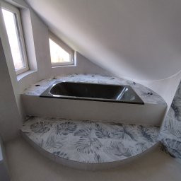 ADMAR ADRIAN MARCISZ - Wykończona łazienka na poddaszu ze skośnym sufitem. Czarna wanna w zabudowie z płytek w liście. Dwa okna w tle. Całość w jasnych, stonowanych barwach.