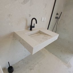 Admar Adrian Marcisz - Elegancka łazienka z beżową umywalką zintegrowaną w blacie z jasnych, kamiennych płytek, czarną baterią i minimalistyczną kabiną prysznicową.