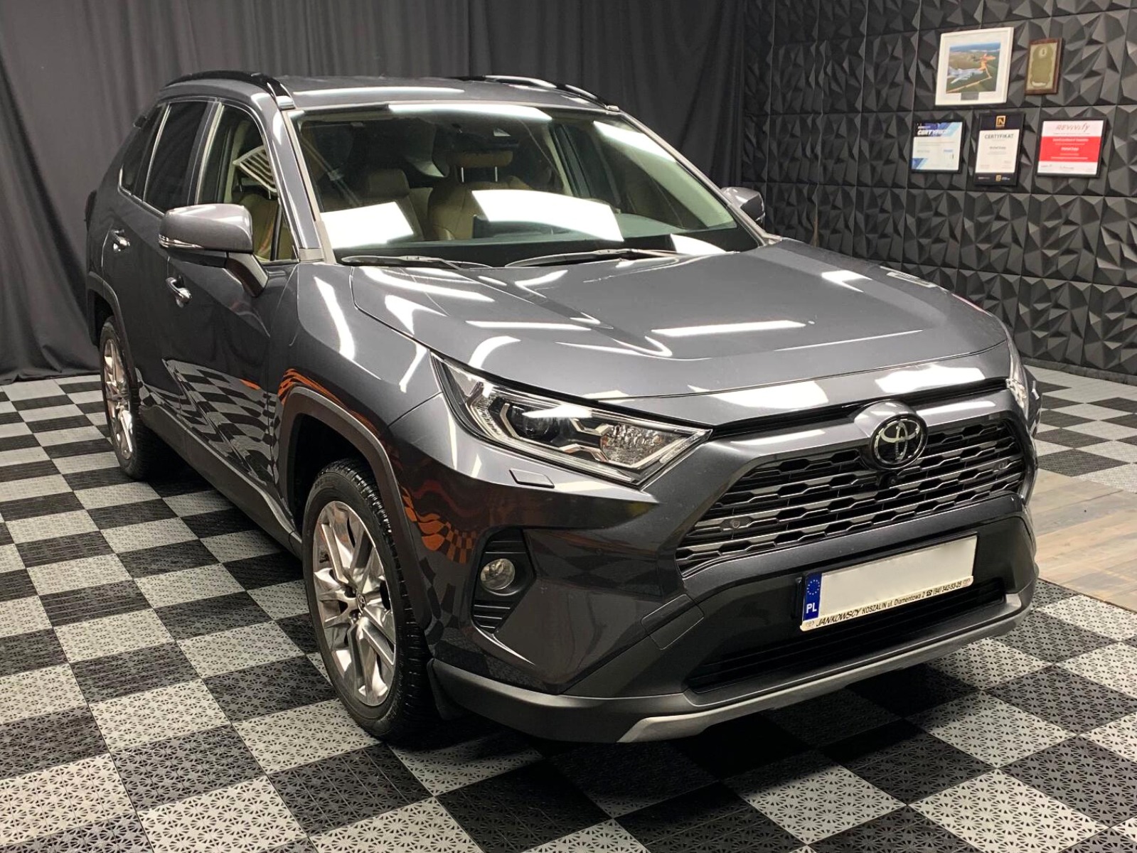 Błyszczący, szary SUV Toyota RAV4 po detailingu, zaparkowany w studiu z czarno-białą podłogą w szachownicę i dekoracyjną ścianą 3D w tle, z widoczną tablicą rejestracyjną.
