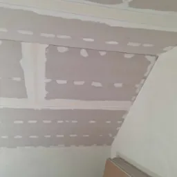 Płyty gipsowo-kartonowe na skośnym poddaszu, widoczne łączenia i szpachlowane miejsca, przygotowane do dalszych prac wykończeniowych.