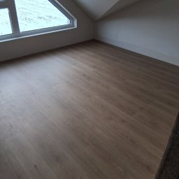 DaRo Bud Dariusz Kucab - Jasne panele podłogowe w pokoju na poddaszu z oknem trójkątnym. Widok na zaśnieżony krajobraz. Minimalistyczne wnętrze, świeżo po remoncie.