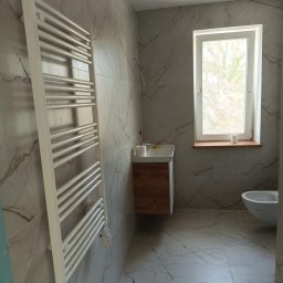 DaRo Bud Dariusz Kucab - Wykończona łazienka z marmurowymi płytkami, grzejnikiem drabinkowym, drewnianą szafką pod umywalką i oknem z drewnianym parapetem. Minimalistyczny design.