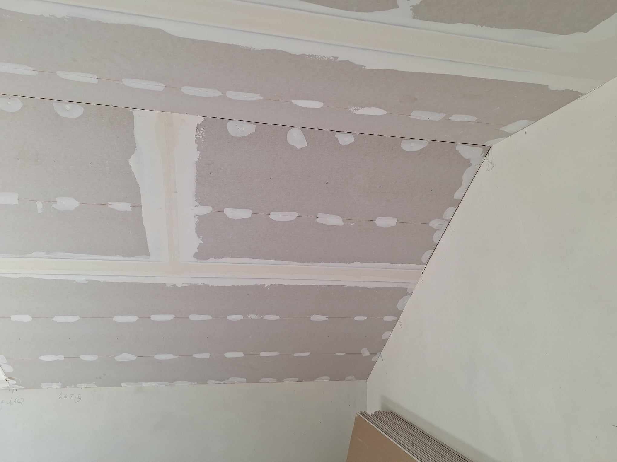 Płyty gipsowo-kartonowe na skośnym poddaszu, widoczne łączenia i szpachlowane miejsca, przygotowane do dalszych prac wykończeniowych.