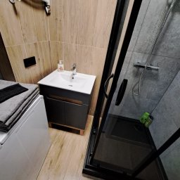 DMT Remonty - Nowoczesna łazienka z kabiną prysznicową z czarnymi ramami, umywalką z szarą szafką, grzejnikiem drabinkowym i pralką z ułożonymi ręcznikami.