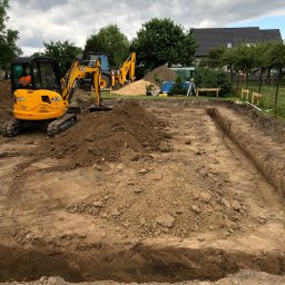 Usługi transportowe i koparka - Żółta koparka JCB i wykopane rowy pod fundamenty na placu budowy z widocznym niwelatorem laserowym w tle.