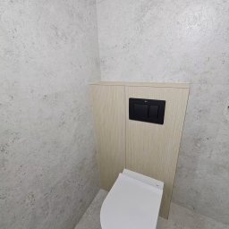 Knechta - Remonty i Wykończenia - Nowoczesna podwieszana toaleta z czarnymi przyciskami spłukującymi, w zabudowie z jasnego drewna, otoczona jasnoszarymi płytkami o teksturze kamienia.