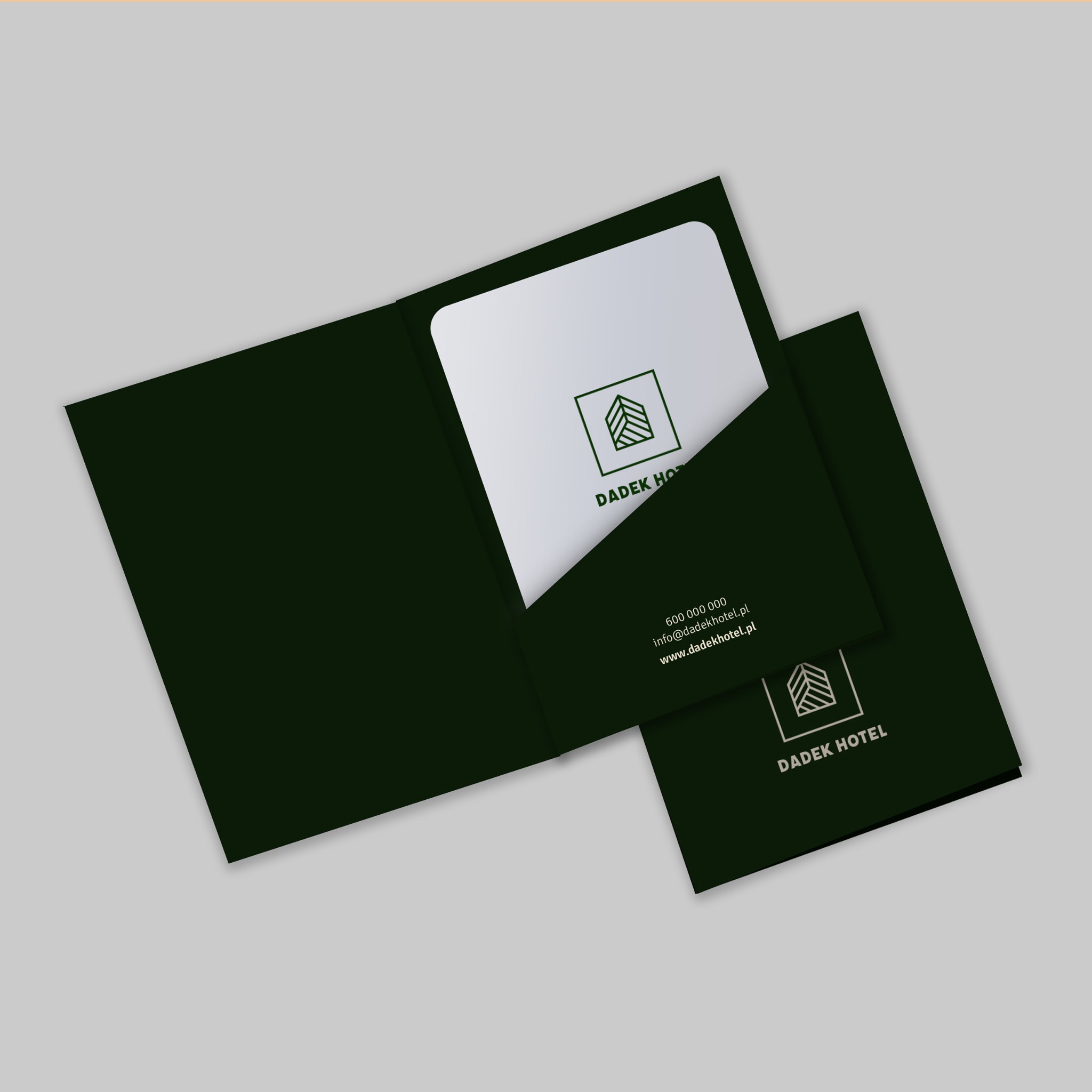 Elegancki, ciemnozielony folder firmowy z wizytówką hotelu, prezentujący logo i dane kontaktowe, ułożony na jasnoszarym tle.