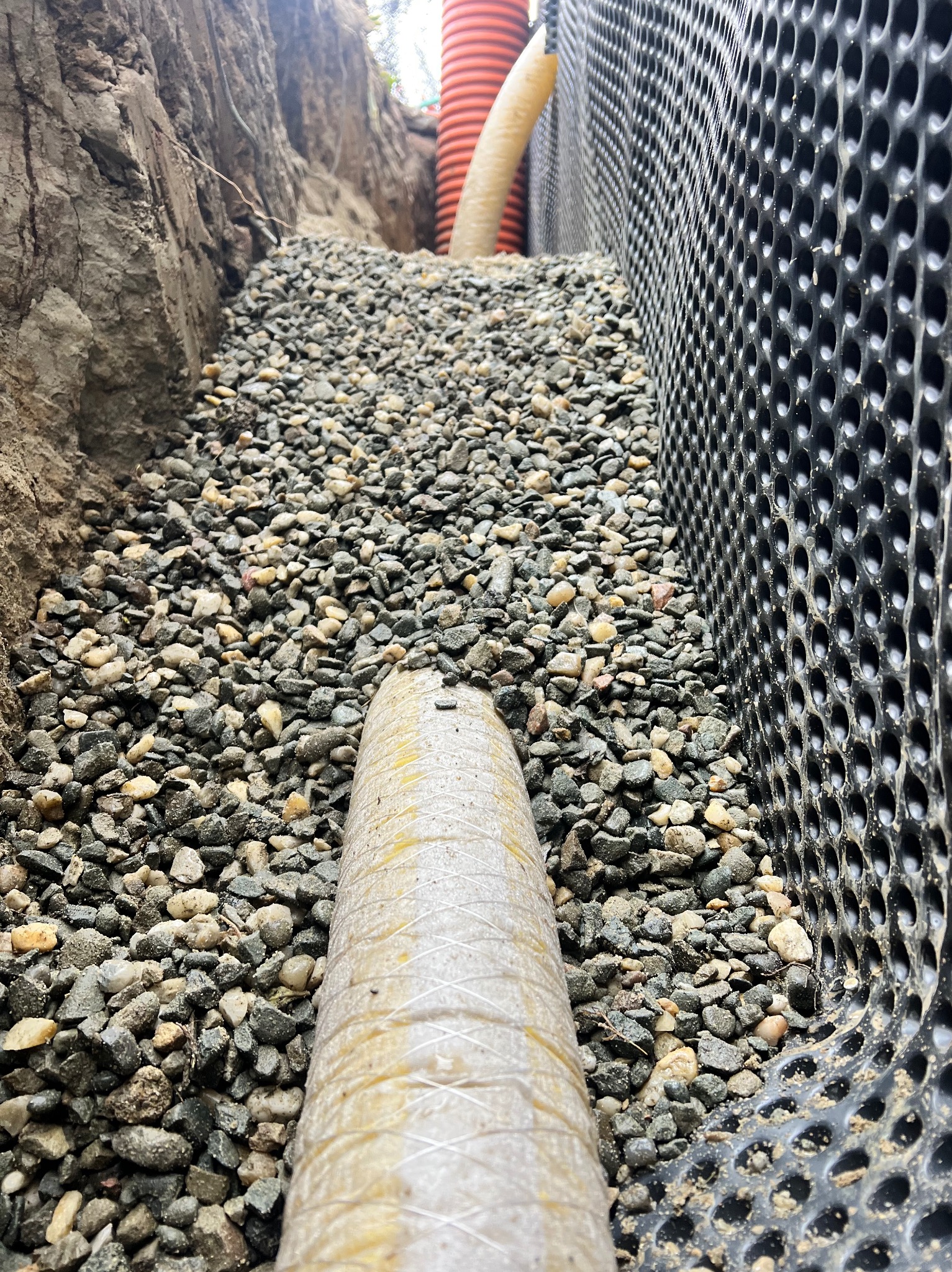 Wykop z warstwą drenażową z kamieni, rurą drenażową w osłonie oraz folią kubełkową przy ścianie wykopu.