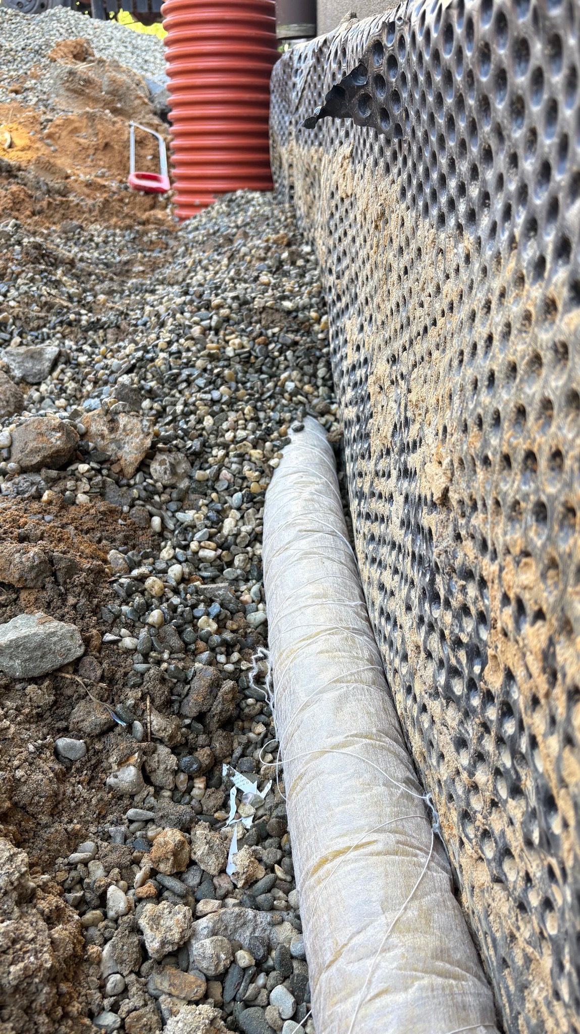 Ochrona fundamentu: folia kubełkowa, obsypka żwirowa, rura drenarska w geowłókninie. Widok z bliska na izolację pionową.