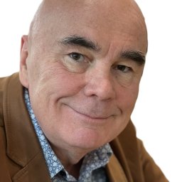 panda.cleaning Dariusz Korczycki - Portret uśmiechniętego mężczyzny w brązowej marynarce i wzorzystej koszuli na białym tle. Widoczne zmarszczki i charakterystyczne brwi.