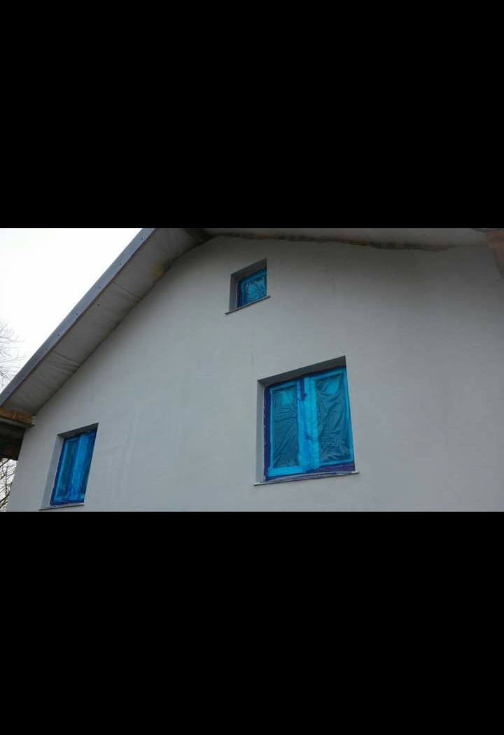 Świeżo otynkowana elewacja domu jednorodzinnego z zabezpieczonymi folią oknami, przygotowana do dalszych prac wykończeniowych.