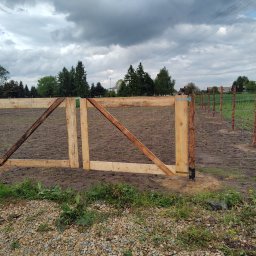 TOMASZ STARZAK GREENBI - Nowo postawiona drewniana brama z furtką i ogrodzeniem z siatki na tle pochmurnego nieba i zieleni.