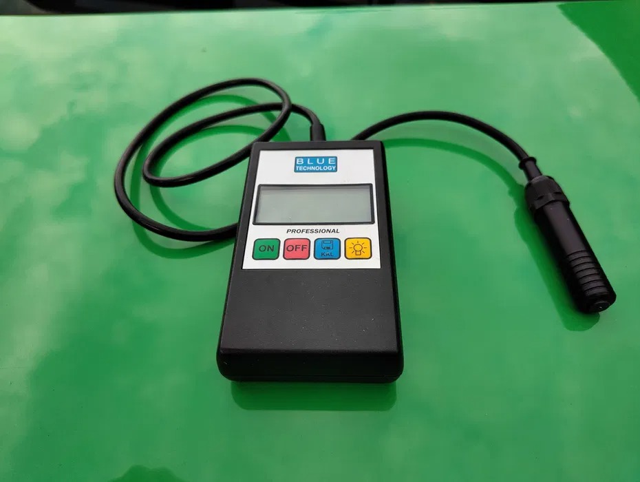 Miernik grubości lakieru Blue Technology Professional na zielonej powierzchni, z widocznym wyświetlaczem, przyciskami i sondą pomiarową.