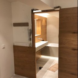 Made - Łazienka w trakcie remontu z drewnianą zabudową, widoczna wanna, umywalka, laser krzyżowy na podłodze i młotek, surowe wykończenie ścian.