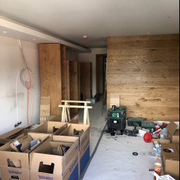 Made - Wnętrze w trakcie prac wykończeniowych: montaż drewnianej zabudowy, widoczne kartony z logo Duravit, narzędzia i kable elektryczne na ścianie.