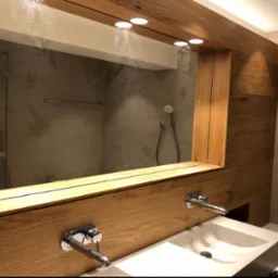 Nowoczesna łazienka z dwiema umywalkami nablatowymi, lustrem w drewnianej ramie i oświetleniem punktowym, widoczny prysznic za szklaną ścianką.