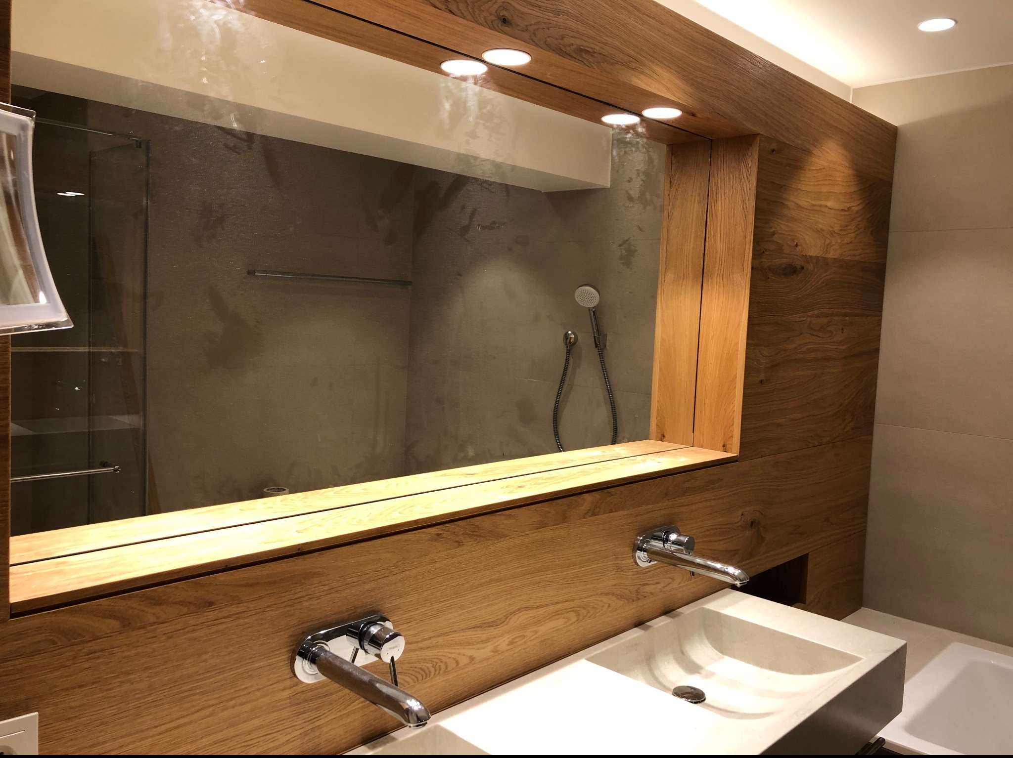 Nowoczesna łazienka z dwiema umywalkami nablatowymi, lustrem w drewnianej ramie i oświetleniem punktowym, widoczny prysznic za szklaną ścianką.