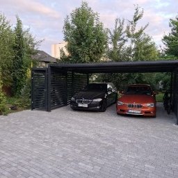 BOL-TAR - Dwa samochody zaparkowane pod nowoczesną, czarną, metalową wiatą garażową z ażurowymi ścianami bocznymi, na posesji z kostki brukowej, otoczonej zielenią.