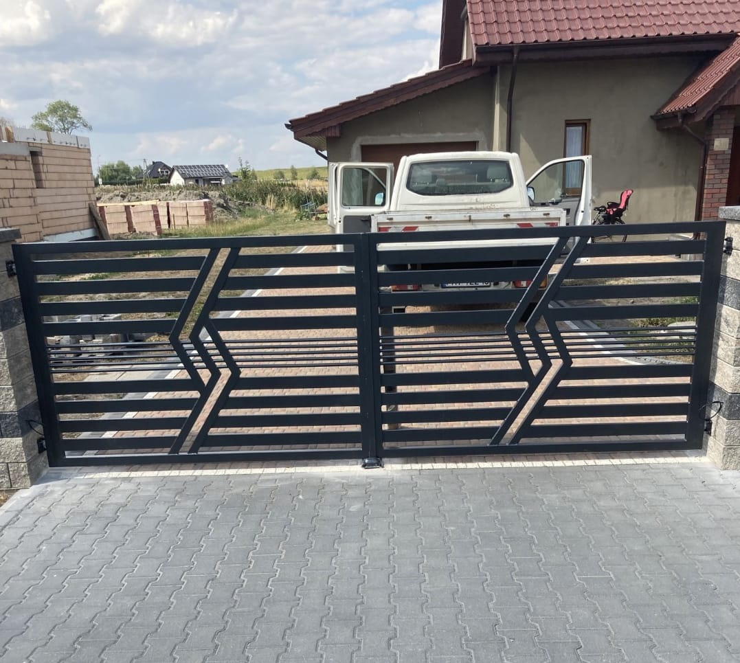 Nowoczesna, czarna brama metalowa z poziomymi przęsłami i geometrycznym wzorem, zamontowana na kamiennych słupkach, z widocznym w tle budynkiem mieszkalnym i samochodem dostawczym z otwartymi...