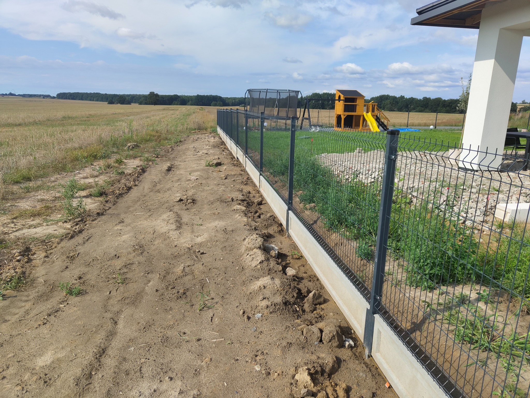 Nowoczesne ogrodzenie panelowe z podmurówką w Tarnowskich Górach, widok z zewnątrz posesji, w tle plac zabaw i pole uprawne.