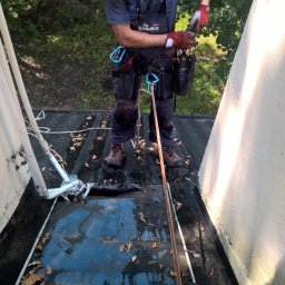 Usługi Wysokościowe, Budowlane i Szkoleniowe EIGER- Piotr Pleszczuk - Pracownik w kombinezonie firmy Śnieżka, zabezpieczony linami, na mokrym dachu z liśćmi, podczas pracy wysokościowej.