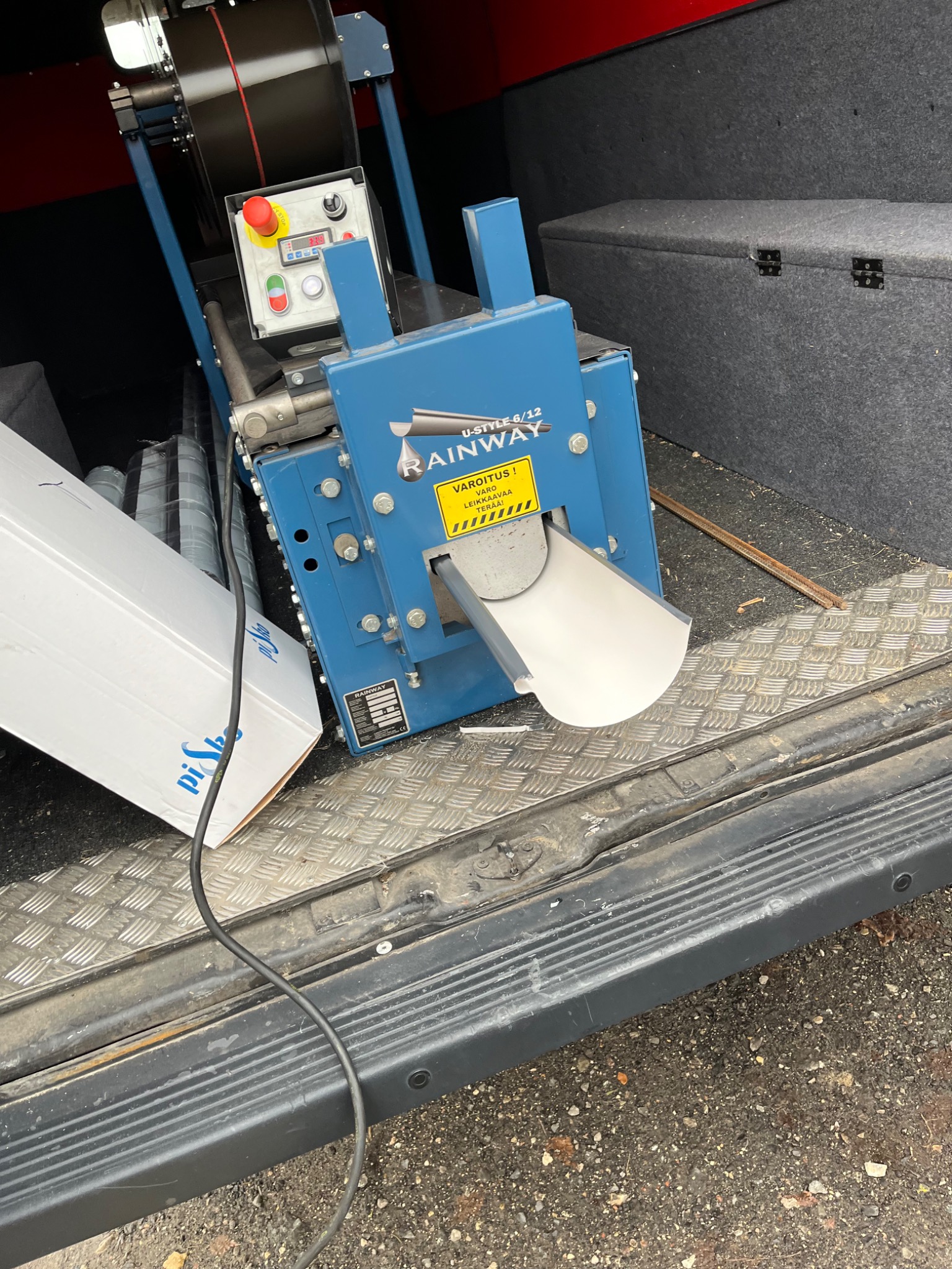 Przenośna, niebieska maszyna Rainway U-Style 6/12 do formowania elementów blaszanych, prawdopodobnie wewnątrz furgonetki, z widocznym fragmentem uformowanej rynny i panelem sterowania.