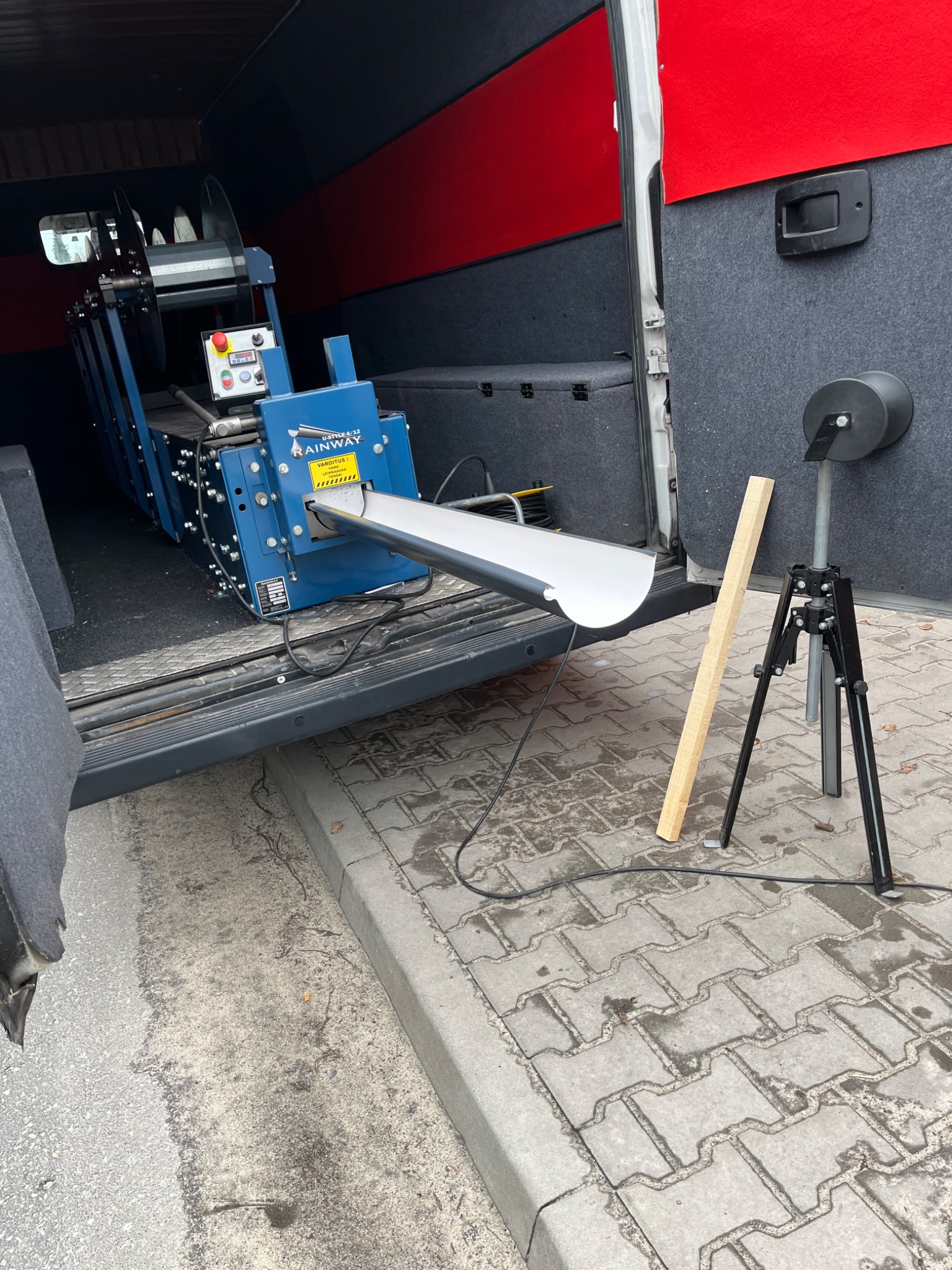 Maszyna do formowania na zimno, zamontowana wewnątrz furgonetki, produkuje profil metalowy. Widoczne są elementy sterujące, rolki prowadzące oraz wysuwający się fragment profilu. Na zewnątrz...