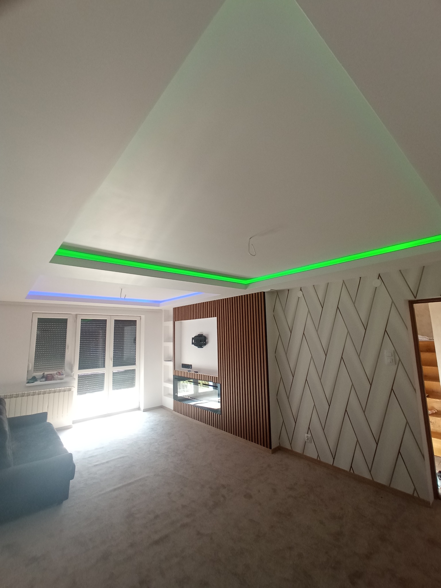 Nowoczesny salon z podwieszanym sufitem z oświetleniem LED, ścianą z lamelami i dekoracyjnym tynkiem. Widoczne tapety i nowa instalacja elektryczna.