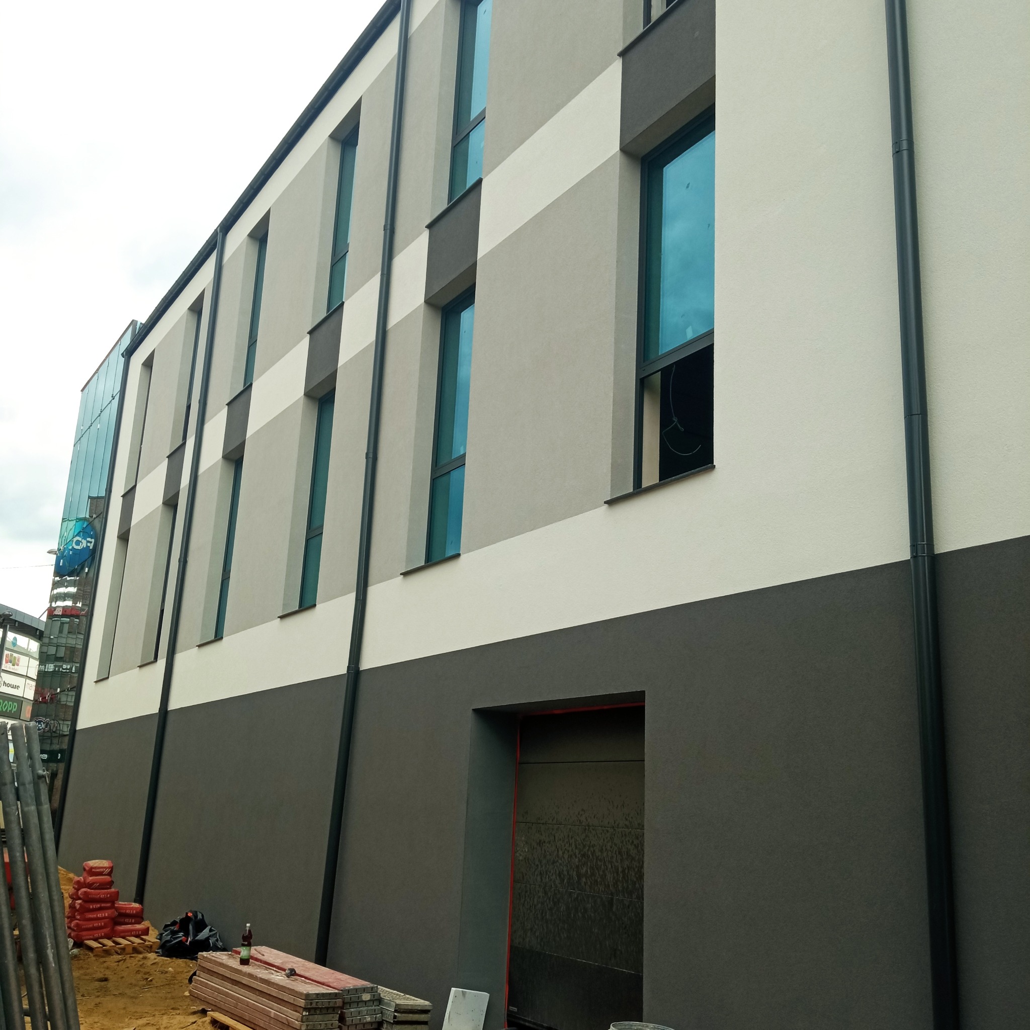 Wielobarwna elewacja budynku z widocznymi oknami i rurami spustowymi. Na pierwszym planie materiały budowlane i rusztowania, sugerujące trwające prace wykończeniowe.