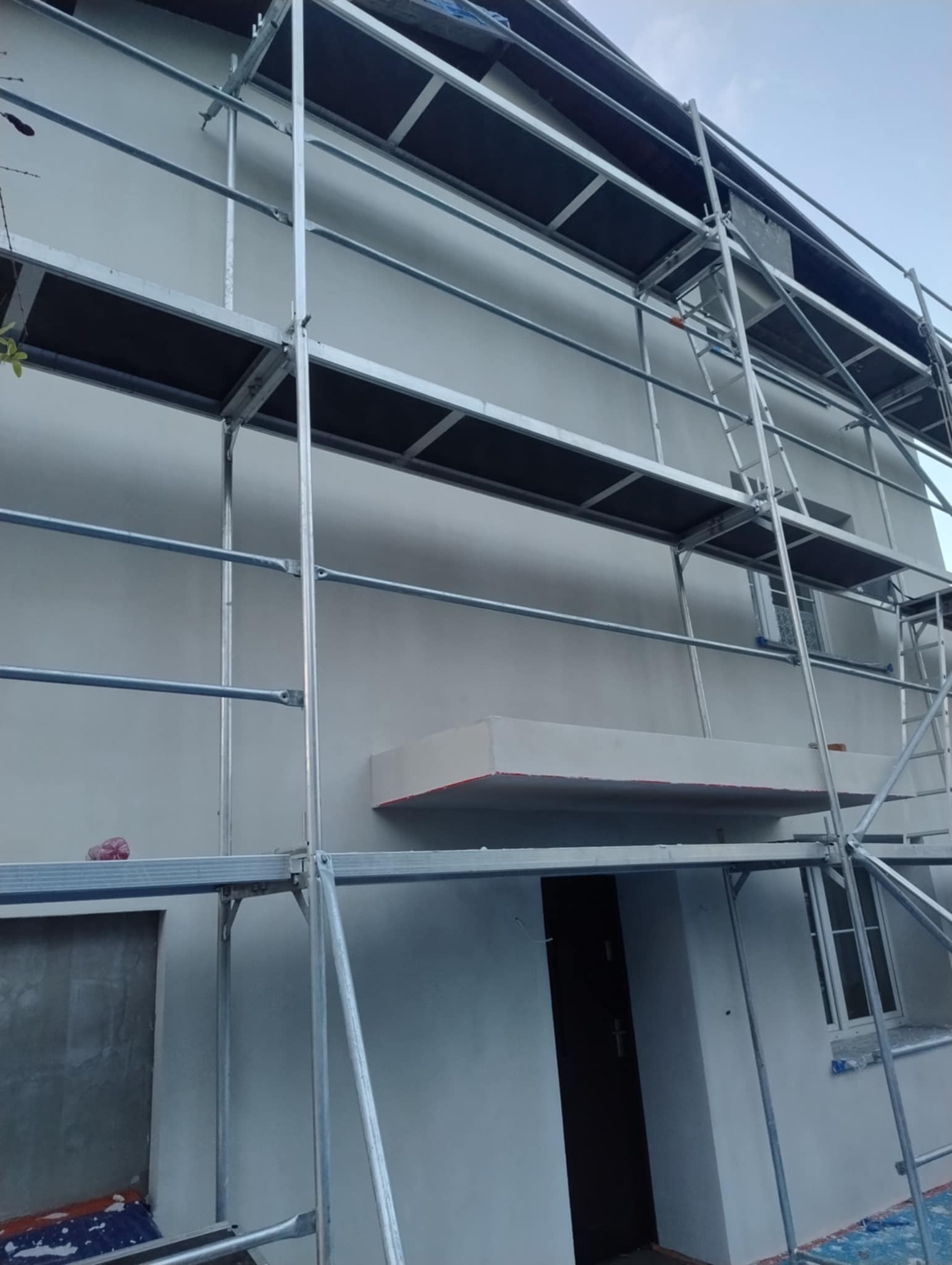 Ocieplona elewacja domu jednorodzinnego w trakcie prac, widoczne rusztowania w Piotrków Trybunalski. Świeżo pomalowana ściana i obudowa wejścia.