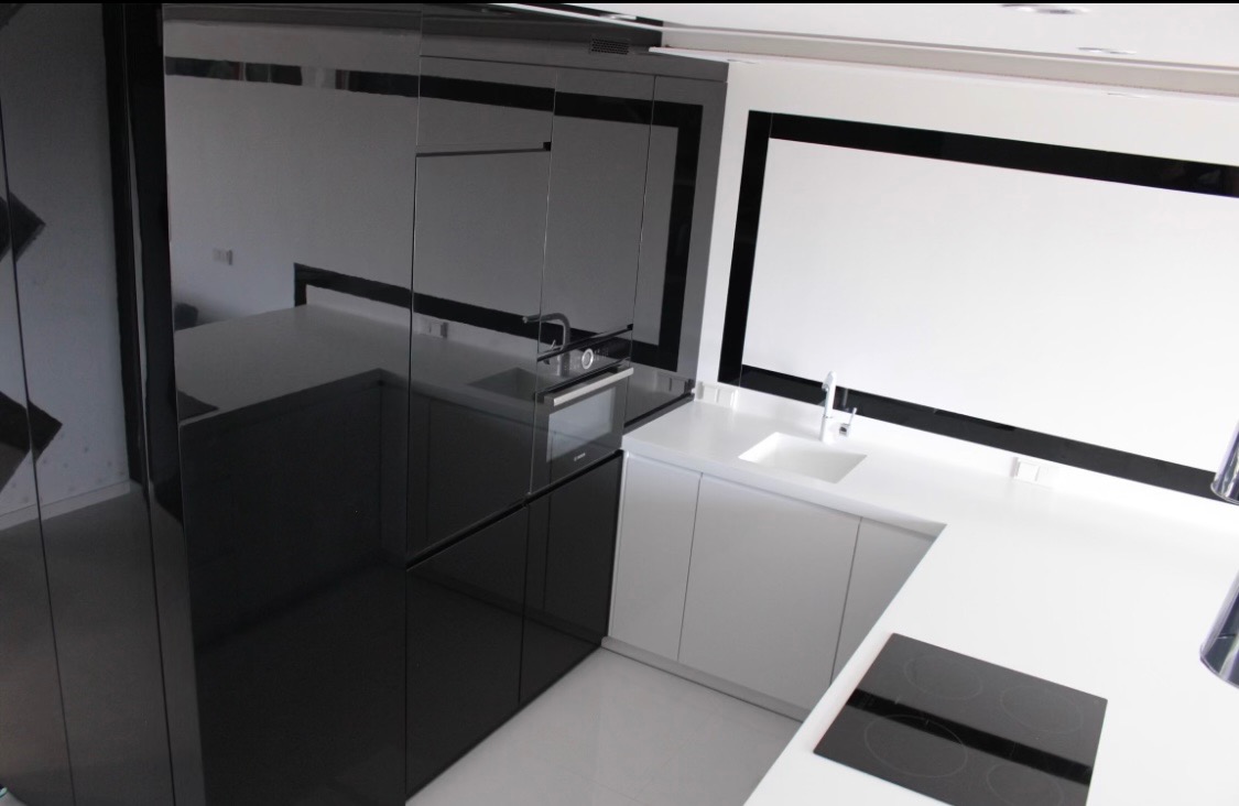 Nowoczesna kuchnia w czarno-białej kolorystyce z błyszczącymi frontami, widoczny zlew, płyta indukcyjna i piekarnik w zabudowie.