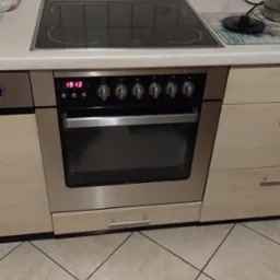 Kuchenka elektryczna Amica z płytą indukcyjną w zabudowie kuchennej z beżowymi płytkami na ścianie i podłodze.