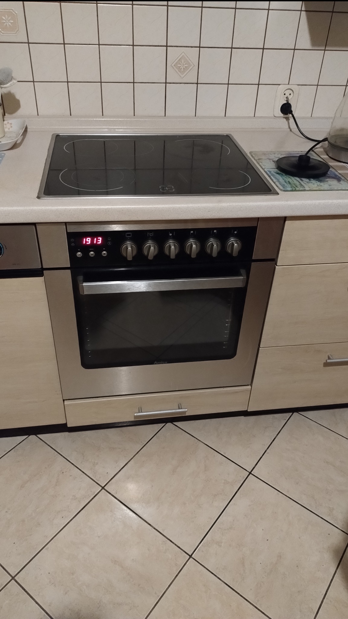 Kuchenka elektryczna Amica z płytą indukcyjną w zabudowie kuchennej z beżowymi płytkami na ścianie i podłodze.