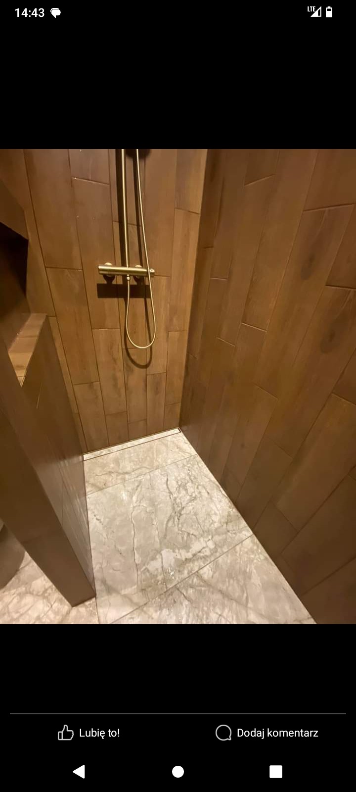 Wykończona kabina prysznicowa z drewnopodobnymi płytkami ściennymi i marmurową posadzką z odpływem liniowym, złota armatura.