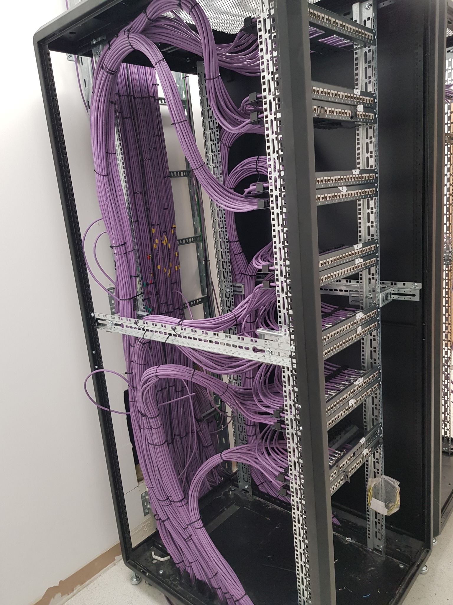 Rząd fioletowych kabli sieciowych starannie ułożonych w szafie rack, z widocznymi panelami krosowniczymi i elementami montażowymi.