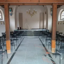 Wnętrze kościoła z nową posadzką z szarego kamienia, rzędy czarnych krzeseł, drewniane kolumny i złoty żyrandol, drabina oparta o podwyższenie o kamiennych schodach, widoczne ślady prac...