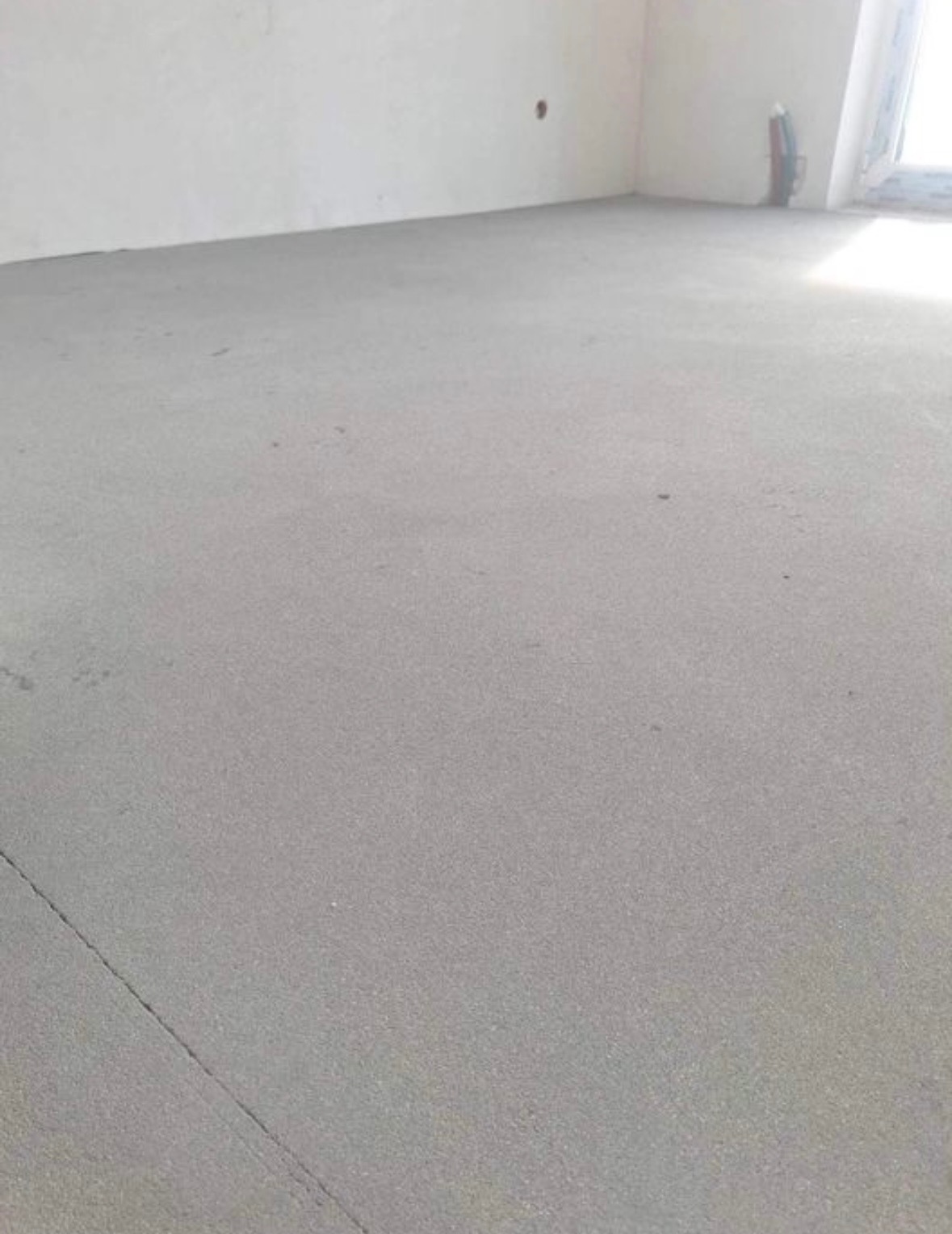 Świeżo wylana, szara posadzka w surowym wnętrzu, widoczne ślady poziomowania i niewielkie niedoskonałości powierzchni.