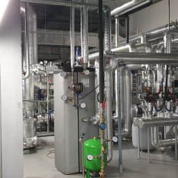 TEWES-KLIMA K.SKOWROŃSKI SPÓŁKA JAWNA - Złożona instalacja przemysłowa z rur, zbiorników i zaworów, pokrytych izolacją termiczną, w hali z szarą posadzką i oświetleniem przemysłowym.