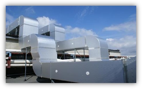 System kanałów wentylacyjnych z blachy ocynkowanej, zamontowany na dachu budynku, widoczny na tle błękitnego nieba z chmurami.