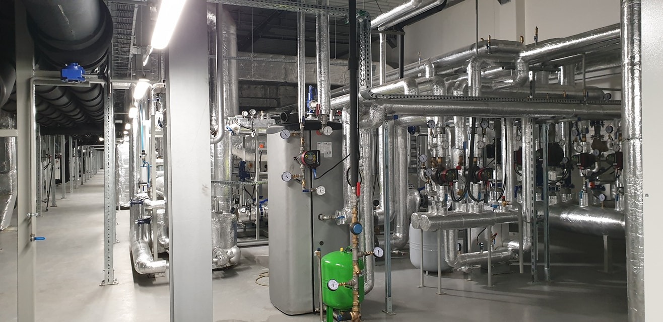 Złożona instalacja przemysłowa z rur, zbiorników i zaworów, pokrytych izolacją termiczną, w hali z szarą posadzką i oświetleniem przemysłowym.