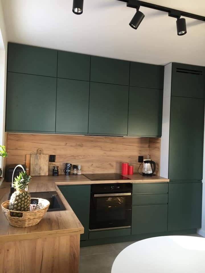 Nowoczesna kuchnia z zielonymi frontami szafek, drewnianym blatem i ananasem w koszyku na blacie.