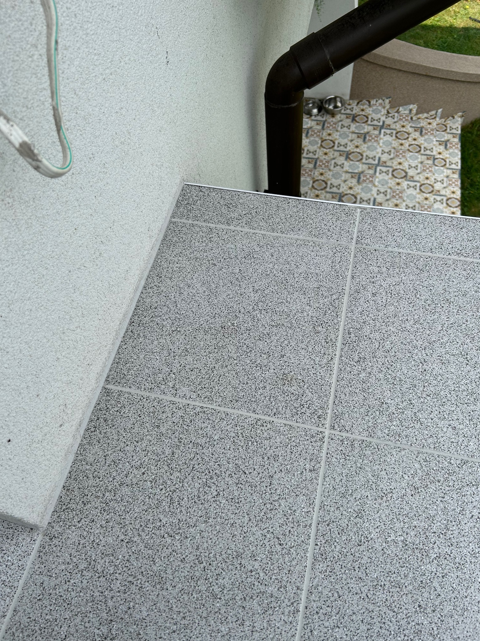 Szare płytki gresowe na schodach zewnętrznych, widoczny fragment elewacji z tynkiem strukturalnym oraz rynna spustowa.