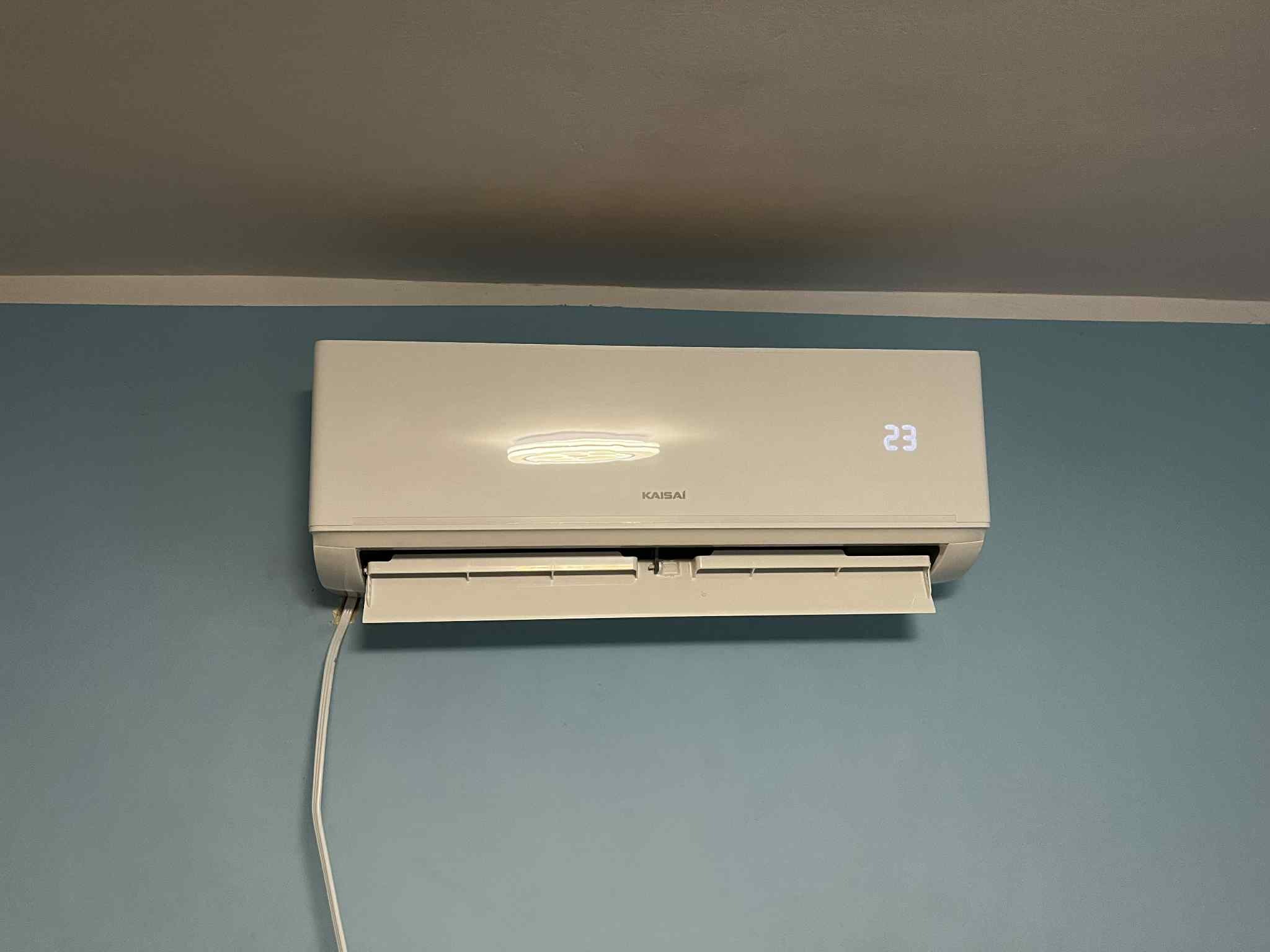 Biała klimatyzacja Kaisai z wyświetlaczem temperatury 23 stopnie, zamontowana na błękitnej ścianie w Bolkowie. Widoczny kabel zasilający.