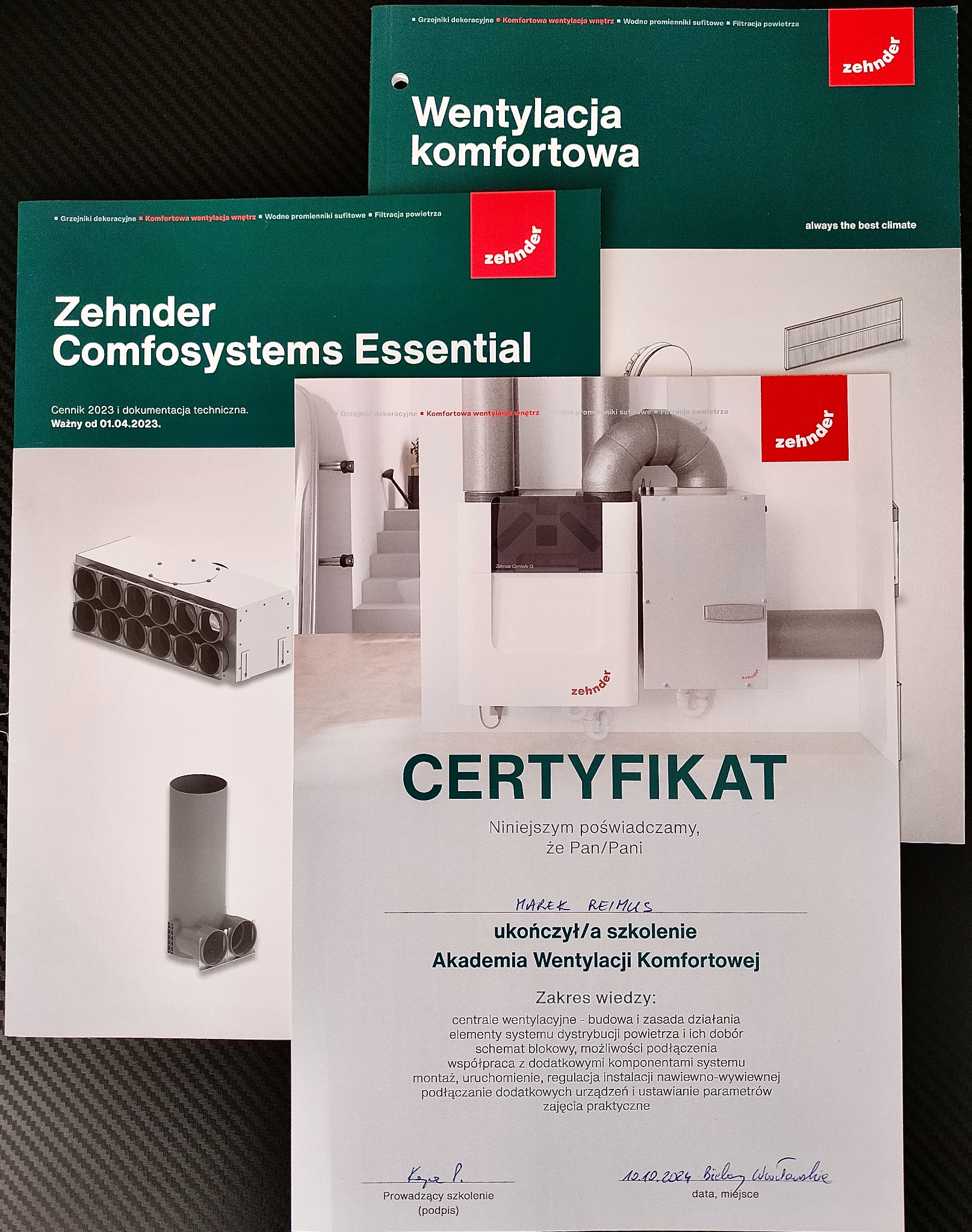 Materiały reklamowe i certyfikat firmy Zehnder dotyczące systemów wentylacji komfortowej, prezentujące centrale wentylacyjne i komponenty, z widocznym certyfikatem ukończenia szkolenia Akademii...