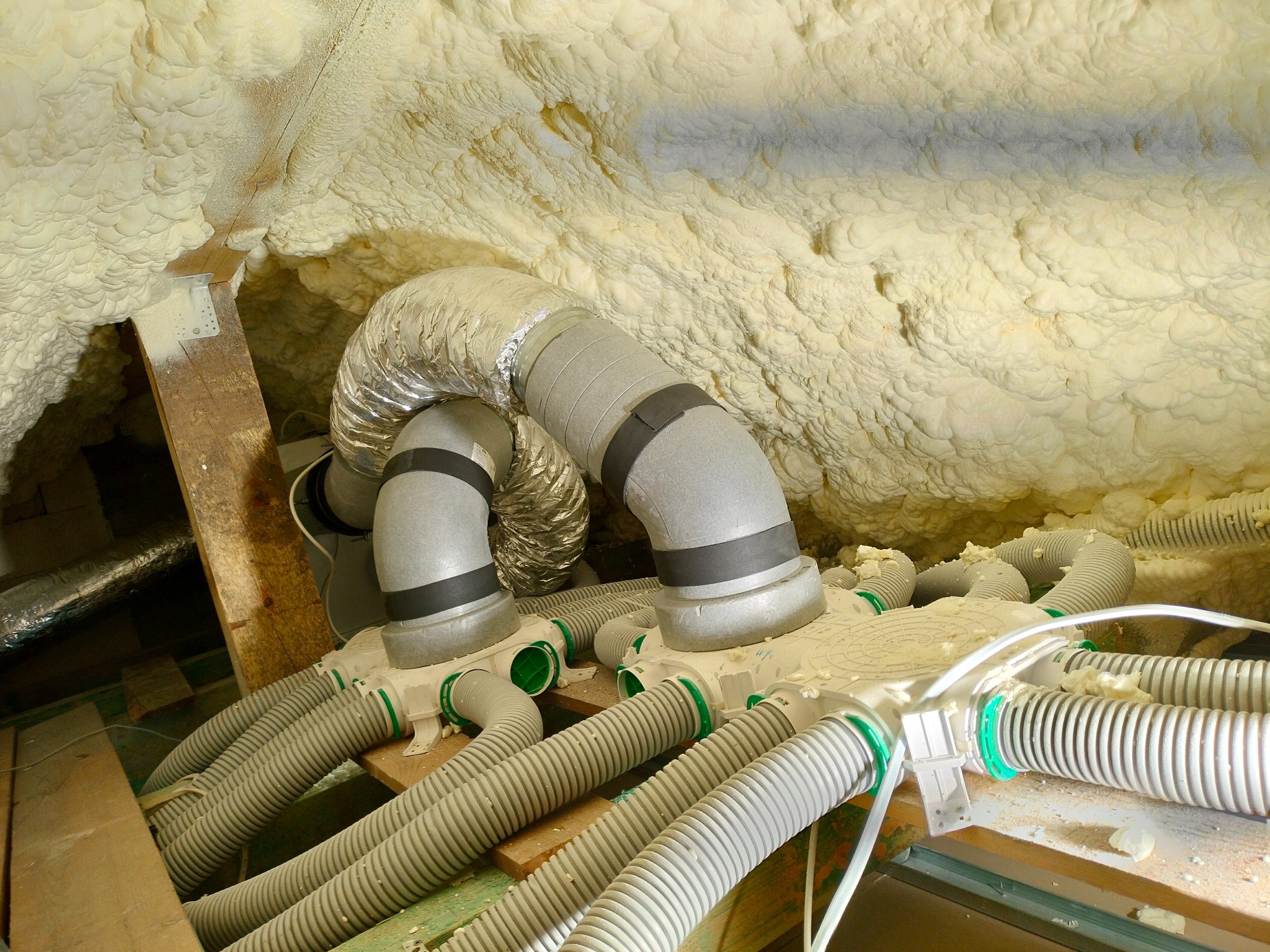 System rozdzielaczowy z szarymi rurami wentylacyjnymi i elastycznymi przewodami, zamontowany w przestrzeni poddasza z izolacją natryskową z pianki poliuretanowej.